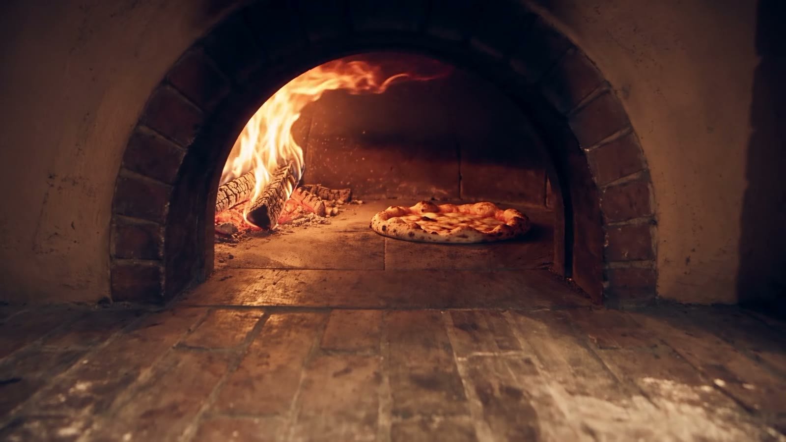 La boca del horno de leña encendida, con una pizza cociéndose sobre el ladrillo.